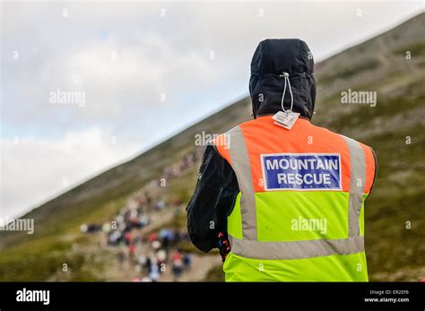 A Man From Mountain Rescue Watches As Hundreds Of People Walk Up A