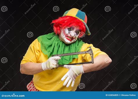 Scary Evil Clown With An Ugly Smile And Saw On A Black Background Stock