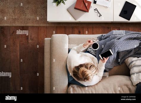 Overhead Shot Looking Down On Woman At Home Lying On Sofa Using Mobile