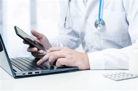 Male Doctor With Laptop And Cellphone At Desk In Medical Office Doctor