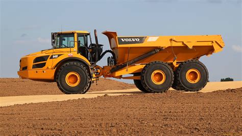 A Large Yellow Dump Truck Driving On Top Of A Dirt Covered Field In