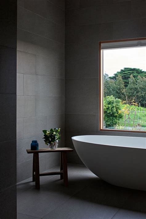 A Large White Bath Tub Sitting Under A Window Next To A Wooden Table