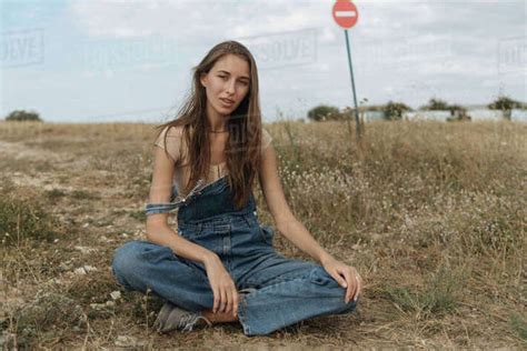 Caucasian Woman Wearing Overalls Sitting In Rocky Field Stock Photo Dissolve