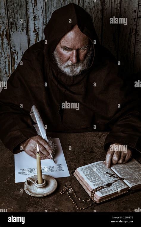 Franciscan Monk Writing In His Cell With His Bible To Hand Stock Photo