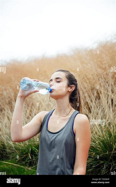 Young Woman Sitting In The Park And Drinking Water After Exercise Stock