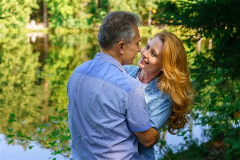 happy mature couple embracing and embracing in thickets headland near lake are stock image