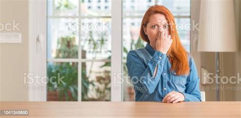 Redhead Woman At Home Smelling Something Stinky And Disgusting Intolerable Smell Holding Breath