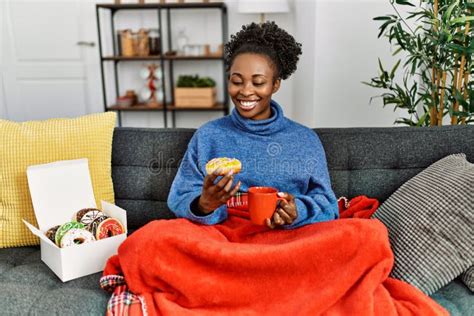 African American Woman Having Breakfast Sitting On Sofa At Home Stock