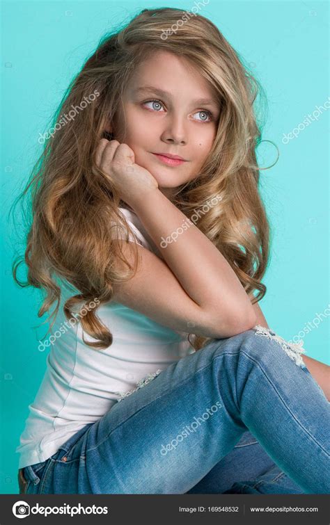 beautiful stunning little blonde girl in denim jeans sitting on a chair on a blue background