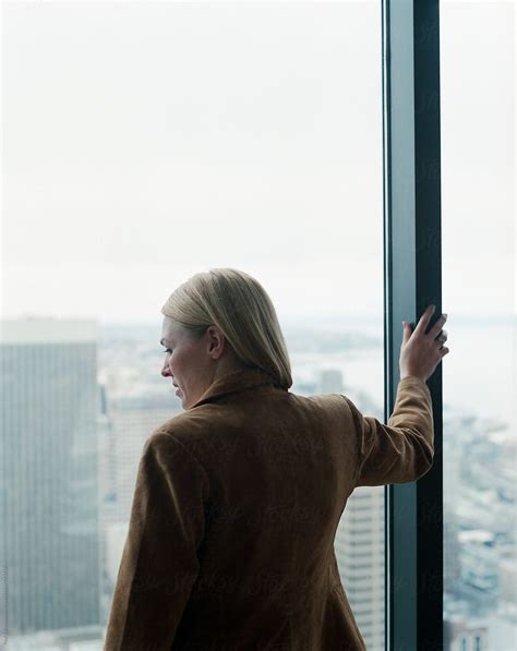 Female Executive Looking Out Large Office Window Towards City Del