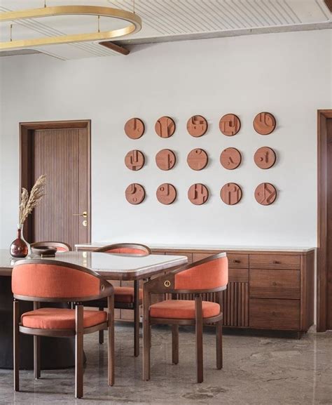 A Dining Room Table With Orange Chairs And Wooden Clocks On The Wall