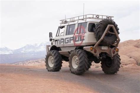 An Off Road Vehicle With Large Tires Driving On A Dirt Road In The Desert