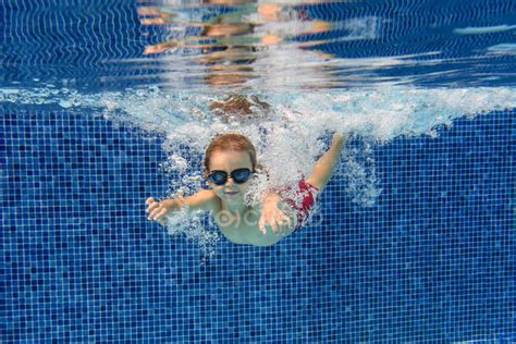 Preschooler In Goggles Swimming In Blue Pool Underwater With Air