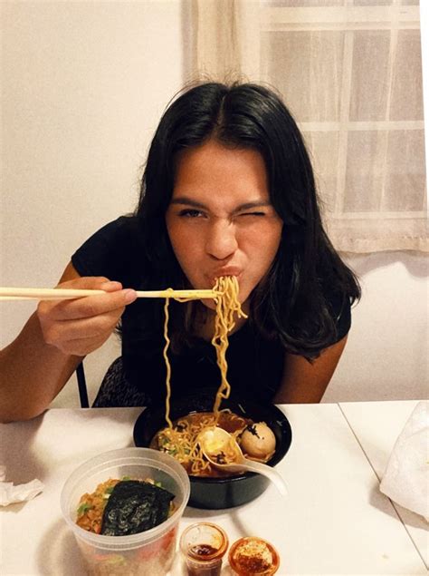 A Woman Is Eating Noodles With Chopsticks At A Table In Front Of Her