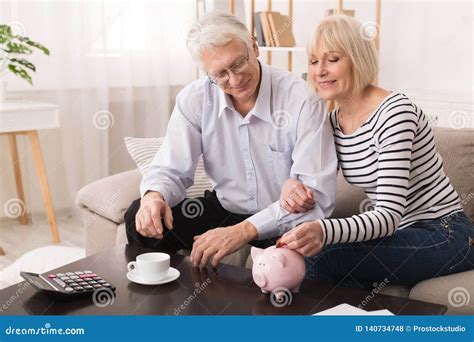 Elderly Couple Saving Money In Piggybank At Home Stock Photo Image Of