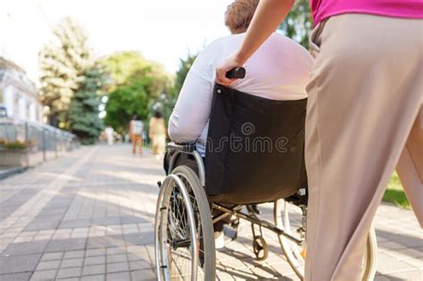 Young Female Caregiver Pushing Wheelchair With Female Person With