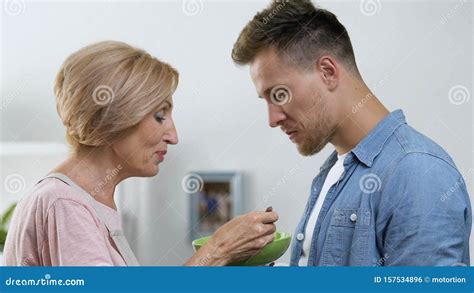 Overprotective Mother Feeding Her Adult Son With Spoon Relations In