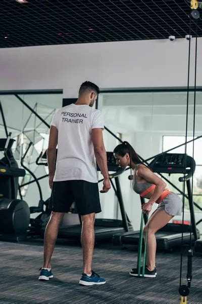 Handsome Trainer Supporting Attractive Sportswoman Lifting Barbell