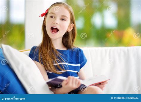 Adorable Little Girl Reading A Book In White Living Room On Beautiful
