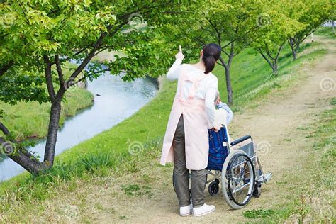 Asian Senior Man Sitting On A Wheelchair With Caregiver Pointing Stock