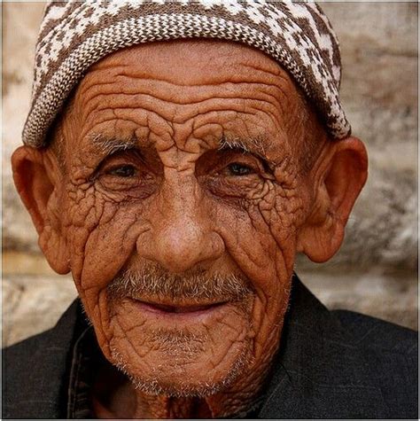 An Old Man With Wrinkles On His Face And Wearing A Knitted Headdress