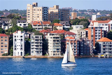 A Sailboat Sailing In The Water Near Some Tall Buildings And Trees On