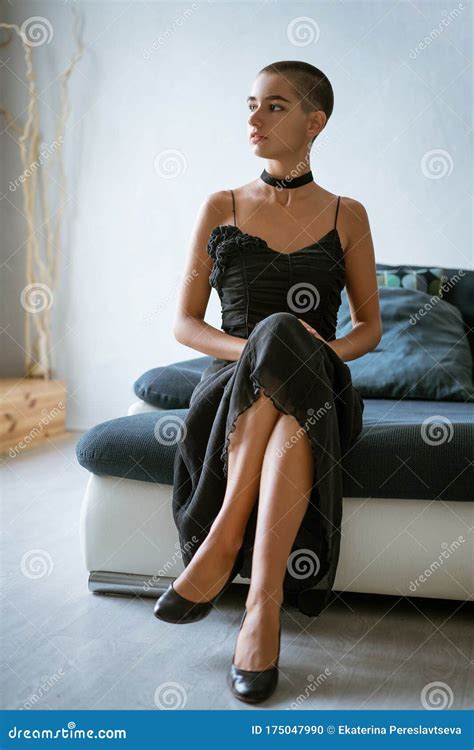 A Young Woman With Short Hair In A Black Dress Is Sitting On The Edge