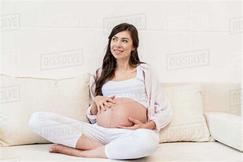 Pregnant Woman Sitting On A Couch In Living Room Touching Her Belly