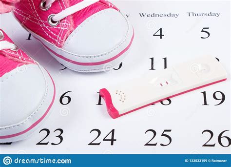 Pregnancy Test With Positive Result And Pink Baby Shoes On Calendar