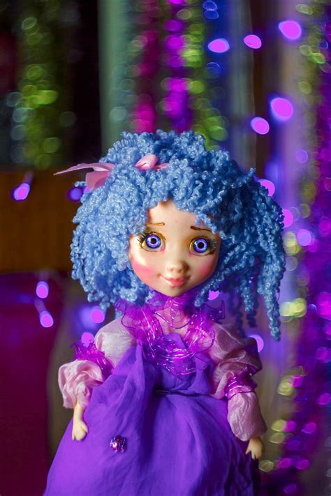 A Doll With Blue Hair Wearing A Purple Dress In Front Of Some Lights