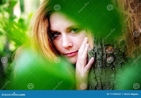 sensual portrait of beautiful red haired woman outdoors under the trees between green leaves