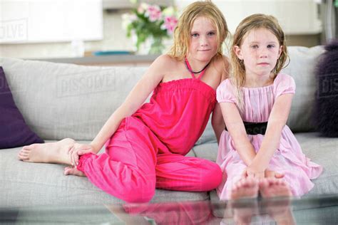 Portrait Of Two Young Sisters Sitting On Sofa Stock Photo Dissolve