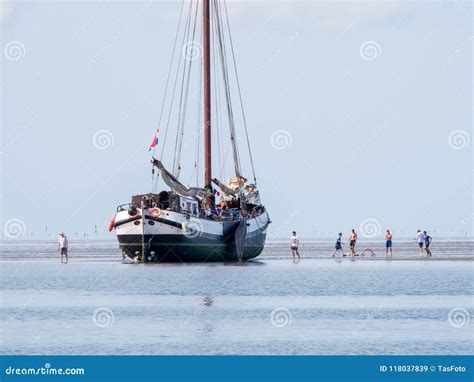 Group Of Youngsters On Sand Flat And Flat Bottom Sailboat At Low