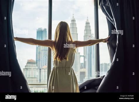 Young Woman Opens The Window Curtains And Looks At The Skyscrapers In