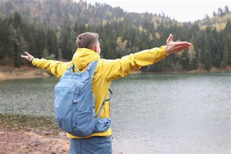 Happy Male Tourist With Open Arms Stands On Shore Of Lake And Looks At