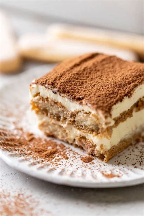 A Slice Of Tiramisu On A White Decorative Plate Three Lady Fingers Rest In The Background