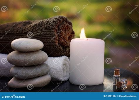 Spa Still Life With Towels A Burning Candle Bath Oil And Massage Stones Against The Backdrop