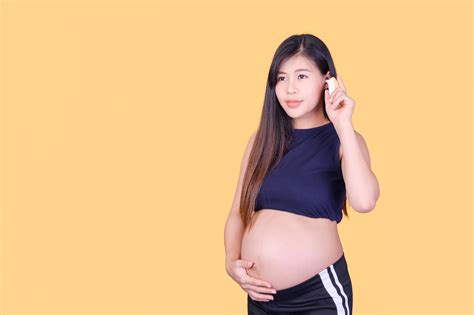 a beautiful pregnant asian woman touches her belly and uses an ear thermometer to measure the