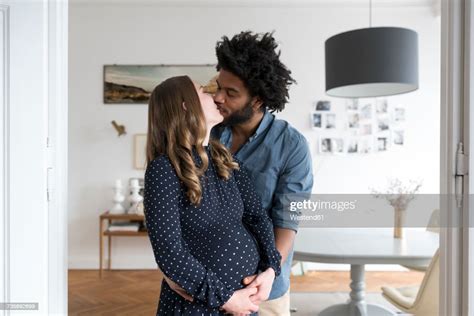 Kissing Pregnant Couple In Living Room Photo Getty Images