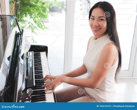 Asian Young Woman Playing Piano Upright In The White Room Stock Photo