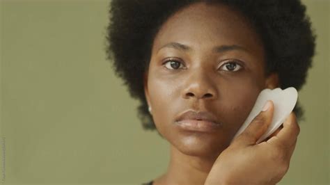 A Young Black Girl Is Doing Facial Massage Using A Gua Sha Stone By