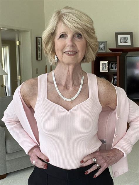 an older woman in a pink sweater and black pants posing for the camera with her hands on her hips