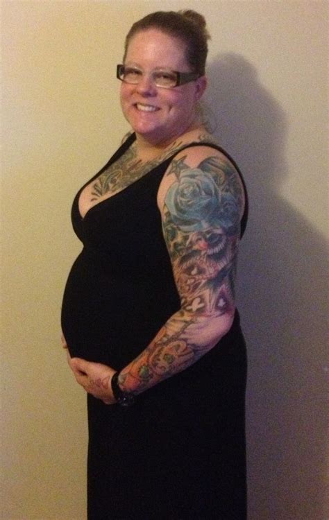 A Pregnant Woman With Tattoos On Her Arms And Belly Standing In Front