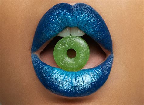 Woman With Blue Shiny Lipstick Holding Green Candy Between Her Teeth