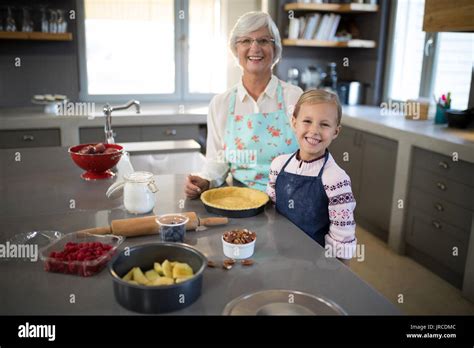 Smiling Grandmother And Granddaughter Posing While Making Pie In The