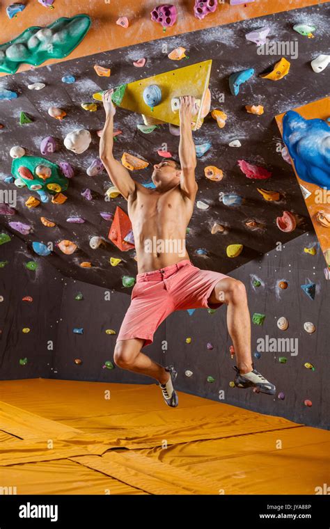 Young Man Bouldering In Indoor Climbing Gym Struggling To Solve