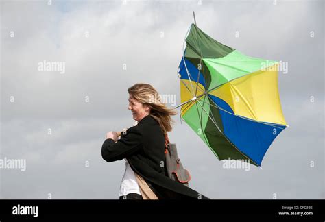Woman Holding Onto Her Umbrella Which Has Blown Inside Out In A High