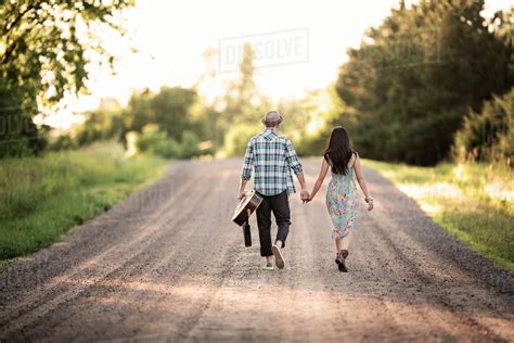 Young Couple Walking Along Dirt Road And Holding Hands Stock Photo