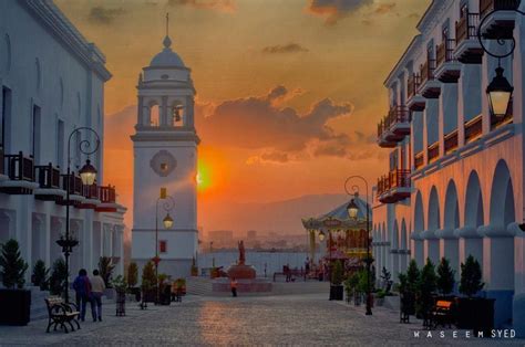 The Sun Is Setting In An Old Town With White Buildings And People