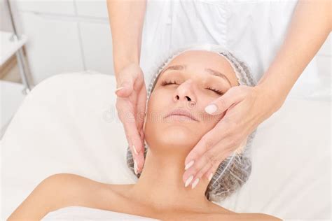 Beautician Massages Cream Mask Into Woman Face Skin For Rejuvenation Procedure In Beauty Salon